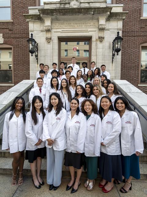 Students wearing white coats standing on the front steps of HSDM