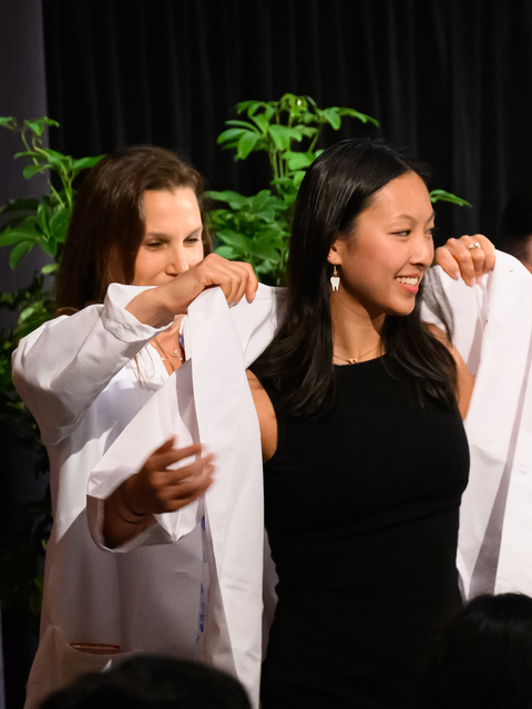 faculty helping students put on their white coats