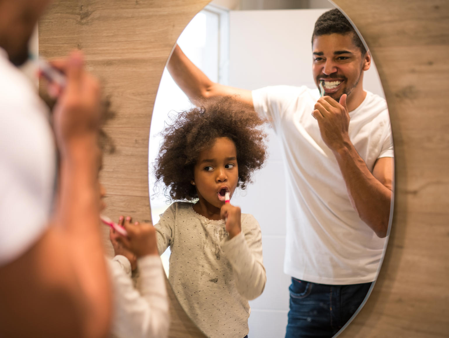 Two family members brushing their teeth while looking in a mirror