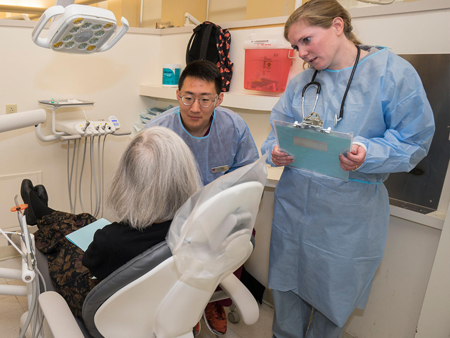 Two clinicians talking to a patient sitting in a dental chair.