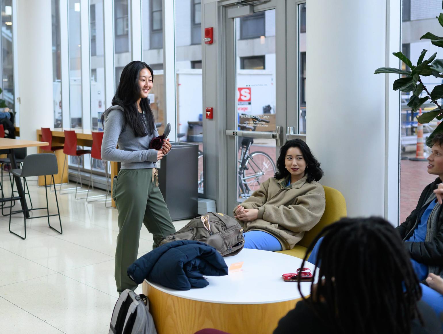 Students gather and talk in a bright common area with tables and seating.