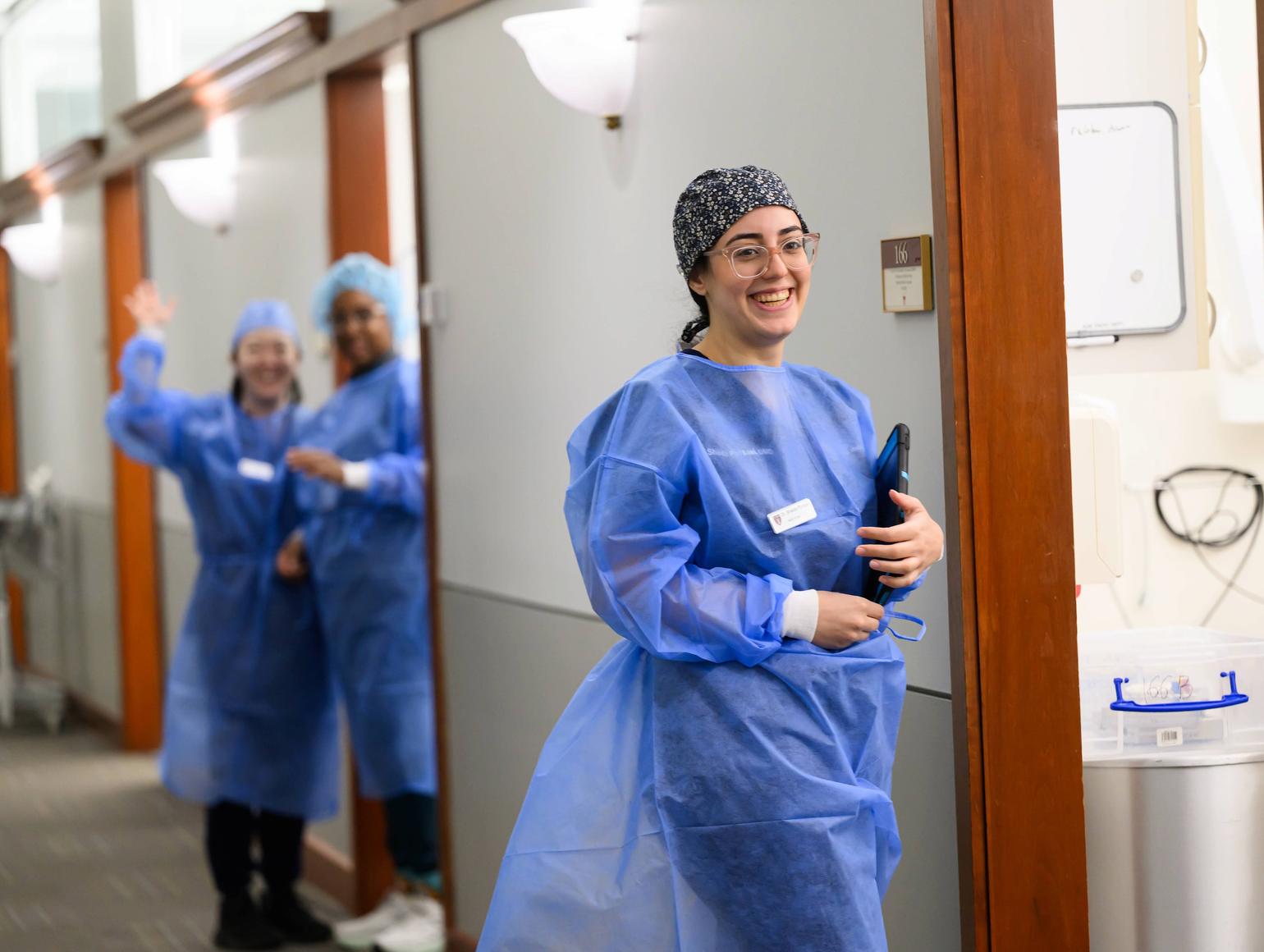 Student in PPE entering an exam room with clinicians also in PPE in background