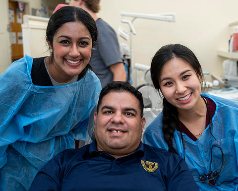 A patient sitting in a dental chair surrounded by two dentists in PPE