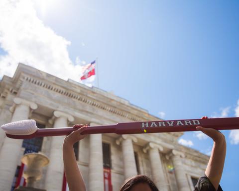 Person holding up a large red toothbrush that reads "Harvard"