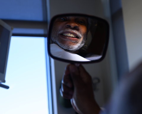 The reflection of a person showing his teeth, looking into a handheld mirror