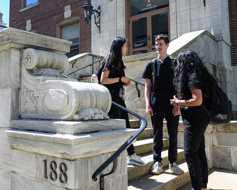 3 students with backpacks standing and talking on the front steps of HSDM main entrance
