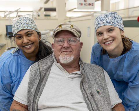 Vet sitting in chair flanked by two female students in PPE