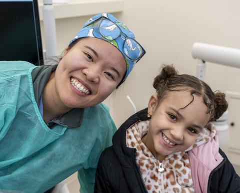 Smiling dental clinician and young patient in a dental exam room.