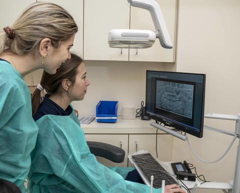Two dental clinicians reviewing a patient's digital panoramic X-ray during orthodontic treatment planning.