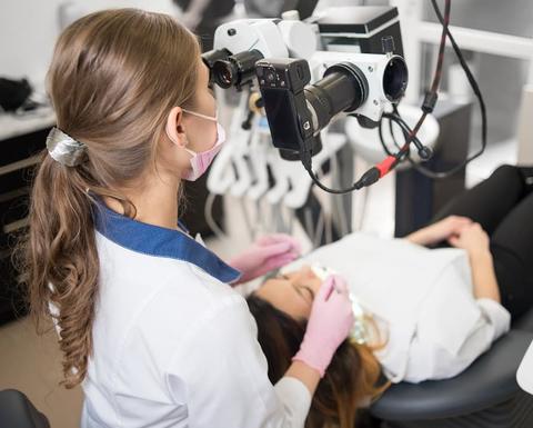 Female dentist with dental tools - microscope, mirror and probe checking up patient teeth at dental clinic office. Medicine, dentistry and health care
