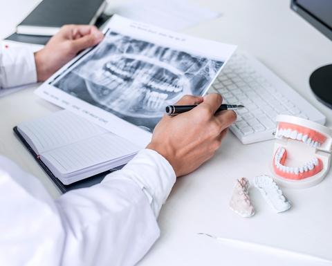 Dentist writing report working with tooth x-ray film, model and equipment used in the treatment of dental and dentistry at workplace
