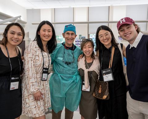 Six HSDM community members gather in a dental teaching clinic during Reunion, including a faculty member wearing surgical attire.