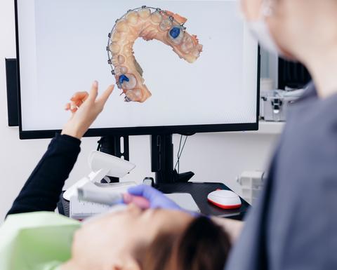 Dentist discussing digital dental 3D scan mold with female patient with braces in dental office