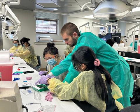 Pre-dental participant practices with dental instruments while an instructor observes in a dental teaching clinic.